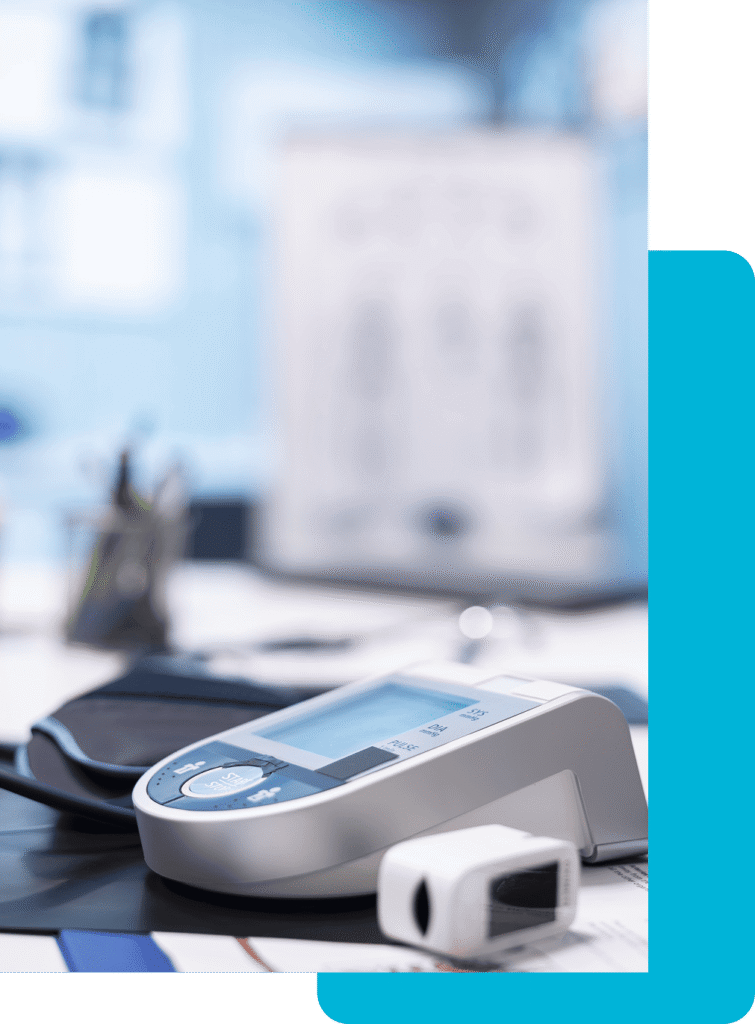 A portable vital signs monitor sits on a table. Office supplies are also on the table. It looks like a doctor's office.