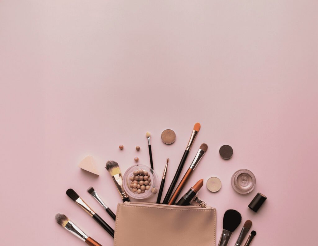 Cosmetic products scattered on a pink background, emerging from a makeup bag.