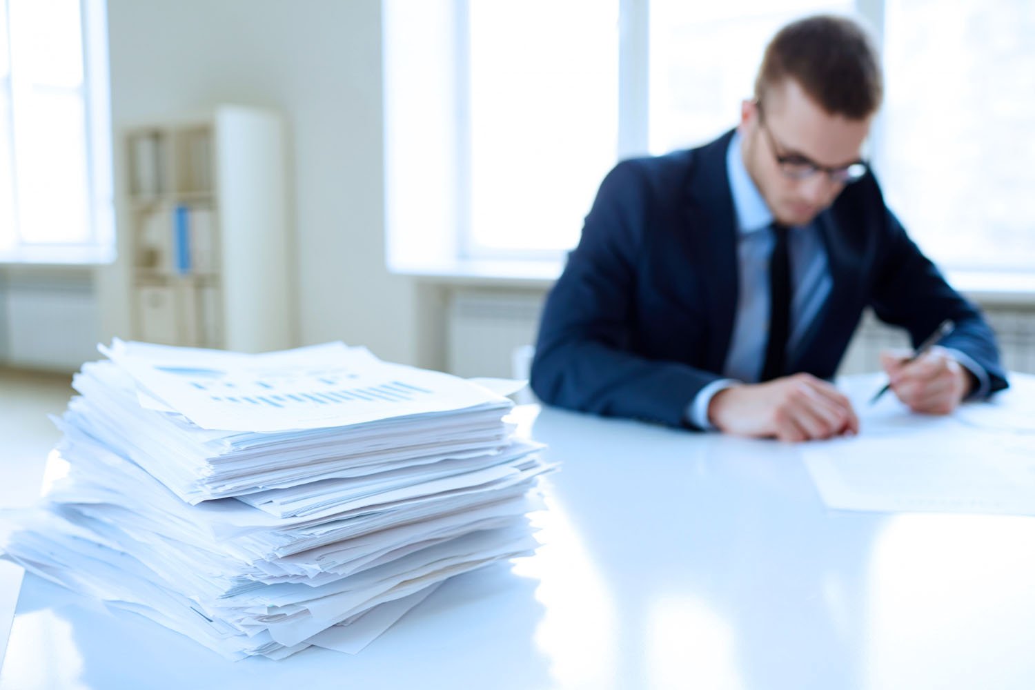 Man at a office desk, looking one document. There is a pile of documents aside him.